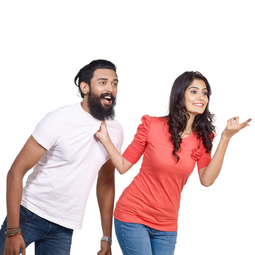 A man and a woman are playfully interacting. The man, wearing a white t-shirt and jeans, is being pulled by the collar by the woman, who is dressed in a red top and blue jeans. Both are smiling, and the woman is gesturing outward with her other hand, as if pointing toward something interesting.