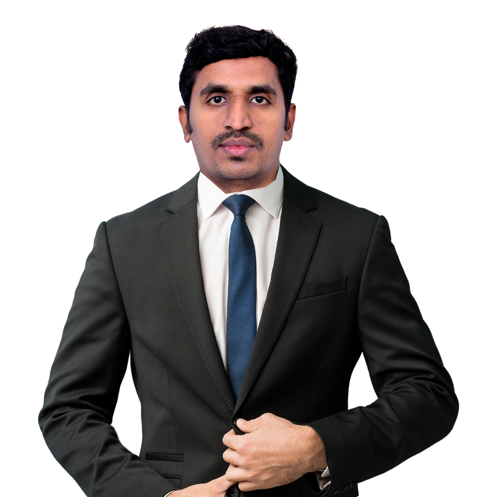 A man with short dark hair and a mustache is wearing a dark suit, white dress shirt, and blue tie. He stands in a professional pose, looking straight at the camera and buttoning his suit jacket with one hand. The background is plain white.